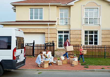 white van outside of fenced-in two story home with family unpacking brown boxes