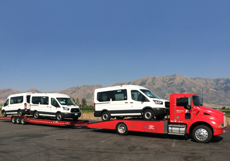 three white vans on a red tractor trailer