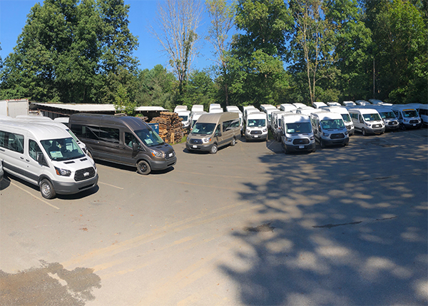 many white vans and one black and one gray van parked in a parking lot
