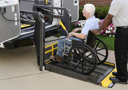 elderly man being wheel-chaired onto a platform into an ADA vehicle by second man